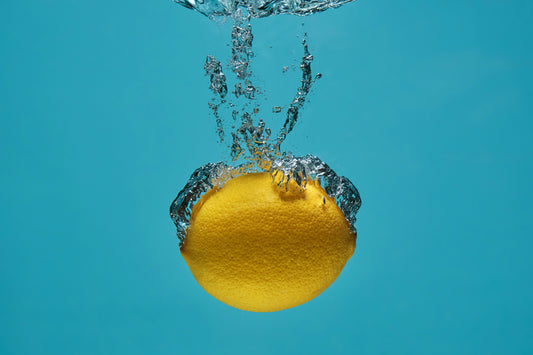 A Lemon, full of electrolytes, falls into some clear water.